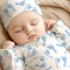 Sleeping Baby Wearing A Blue Footprint Onesie And Matching Hat.
