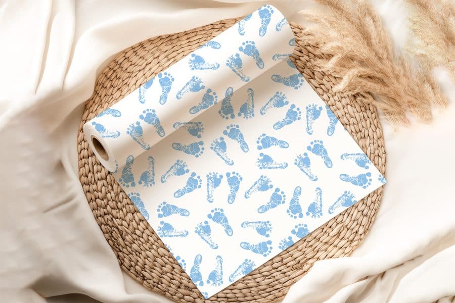 A Roll Of Baby Blue Footprint Patterned Wrapping Paper Sits On A Woven Placemat.