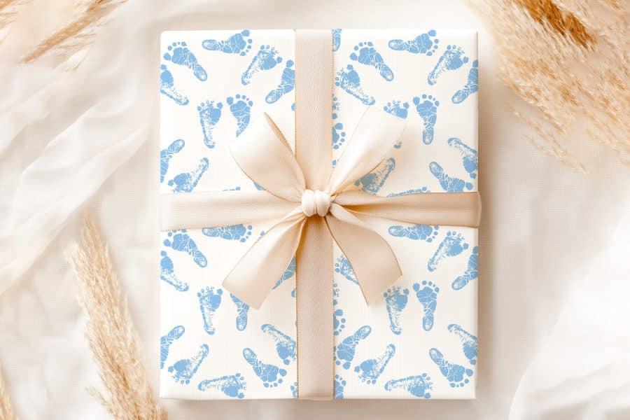 A Gift Wrapped In White Paper With A Pattern Of Light Blue Baby Footprints And Tied With A Beige Ribbon.