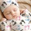 Sleeping Baby Wearing A Footed Onesie And Hat With A Footprint Pattern.