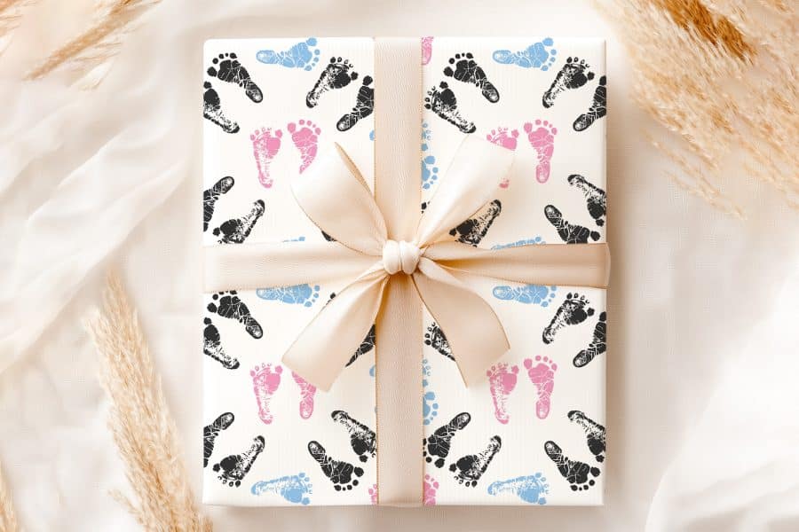 A Gift Wrapped In Paper With Pink, Blue, And Black Baby Footprints, Tied With A Beige Ribbon.