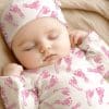 Sleeping Baby Wearing A Pink Footprint Onesie And Matching Hat.