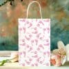 White Gift Bag With Pink Baby Footprints, Next To Pink Flowers.