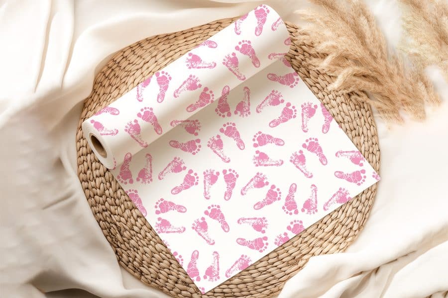 A Roll Of Wrapping Paper Featuring A Repeating Pattern Of Pink Baby Footprints On A White Background.