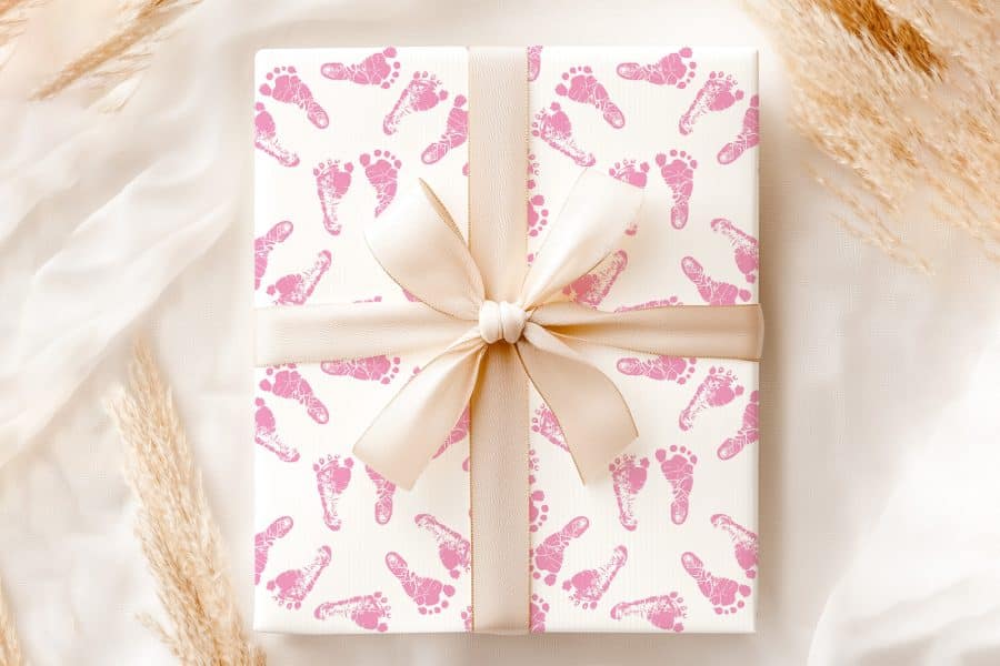 A Gift Wrapped In Pink Baby Footprints Wrapping Paper With A Beige Ribbon.