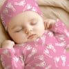 Sleeping Baby Wearing A Pink Footed Pajamas And Matching Hat.