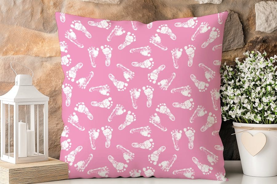 Pink Square Pillow With A Pattern Of White Baby Footprints.