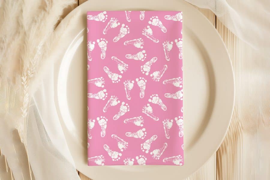 Pink Napkin With A White Baby Footprint Pattern On A Plate.