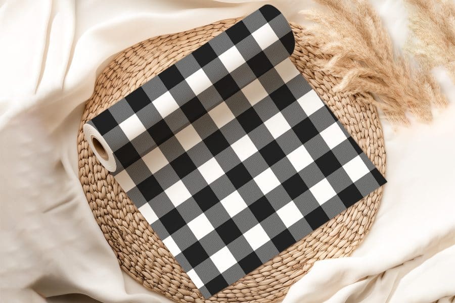 A Roll Of Black And White Buffalo Plaid Fabric On A Woven Mat.