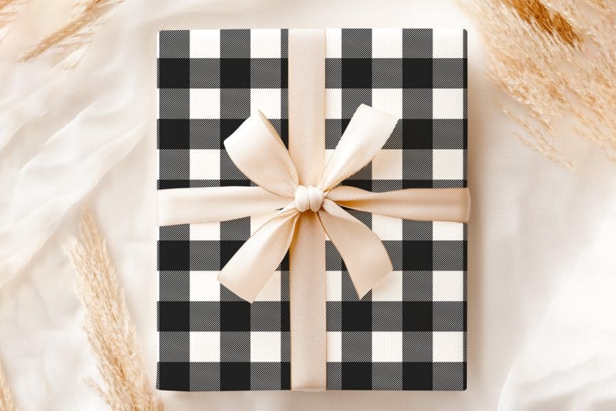A Gift Wrapped In Black And White Buffalo Plaid With A Beige Ribbon.