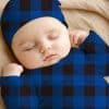 Sleeping Baby Wearing A Blue And Black Plaid Onesie And Matching Hat.