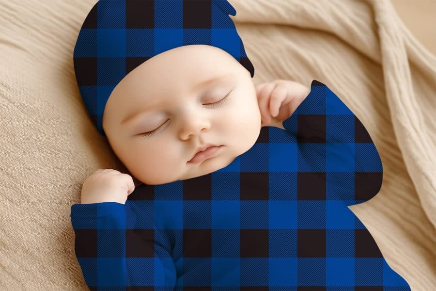 Sleeping Baby Wearing A Blue And Black Plaid Onesie And Matching Hat.