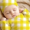 Sleeping Baby Wearing A Yellow And White Gingham Outfit.