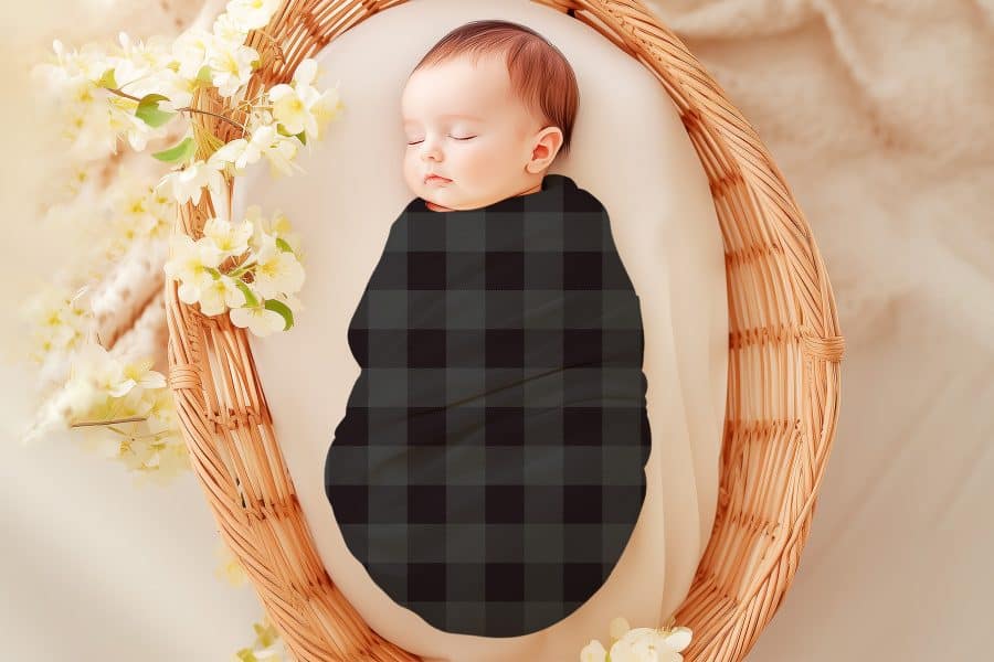 Sleeping baby swaddled in a dark gray and black plaid blanket.