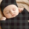 Sleeping Baby Wearing A Dark Gray And Black Plaid Onesie And Matching Hat.
