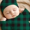 Sleeping Baby Wearing A Green And Black Buffalo Plaid Hat And Sleeper.