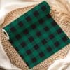 Roll Of Dark Green And Black Buffalo Plaid Fabric On A Woven Placemat.