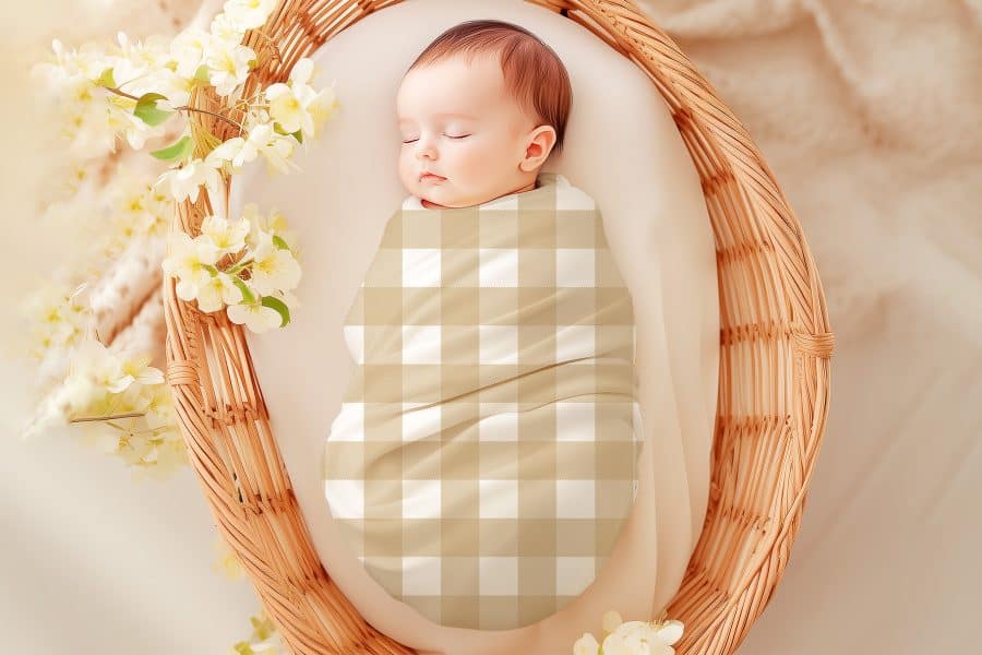 Sleeping baby wrapped in a tan and white gingham swaddle, nestled in a wicker basket.