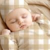 Sleeping Baby Wearing A Beige And White Gingham Outfit.
