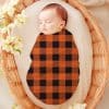 Sleeping Baby Swaddled In An Orange And Black Buffalo Plaid Blanket.