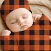 Sleeping Baby Wearing An Orange And Black Buffalo Plaid Outfit.