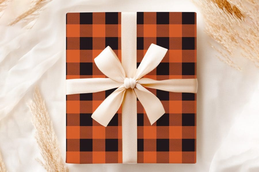 A Gift Wrapped In Orange And Black Buffalo Plaid With A Cream-Colored Ribbon.