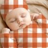 Sleeping Baby Wearing An Orange And White Gingham Outfit.