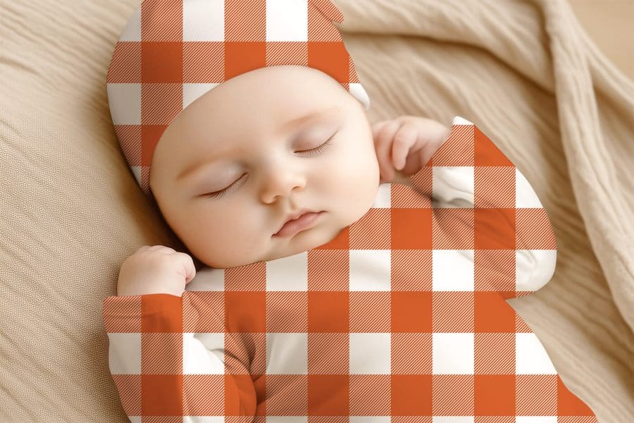 Sleeping Baby Wearing An Orange And White Gingham Outfit.