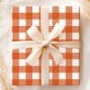 A Gift Box With An Orange And White Checkered Pattern, Tied With A Cream-Colored Ribbon.