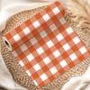 Roll Of Orange And White Gingham Fabric On A Woven Placemat.