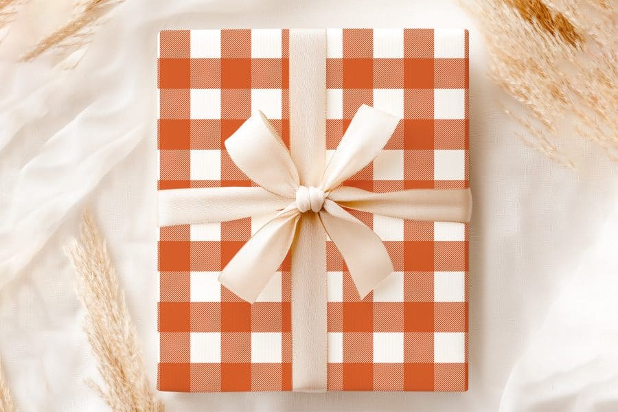 A Gift Box With An Orange And White Checkered Pattern, Tied With A Cream-Colored Ribbon.