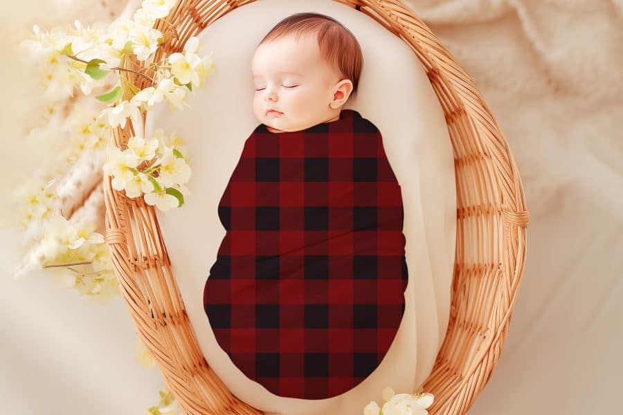 Sleeping baby swaddled in a red and black buffalo plaid blanket.