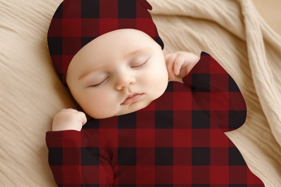 Sleeping Baby Wearing A Red And Black Buffalo Plaid Onesie And Matching Hat.