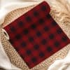 A Roll Of Red And Black Buffalo Plaid Fabric Rests On A Woven Mat.