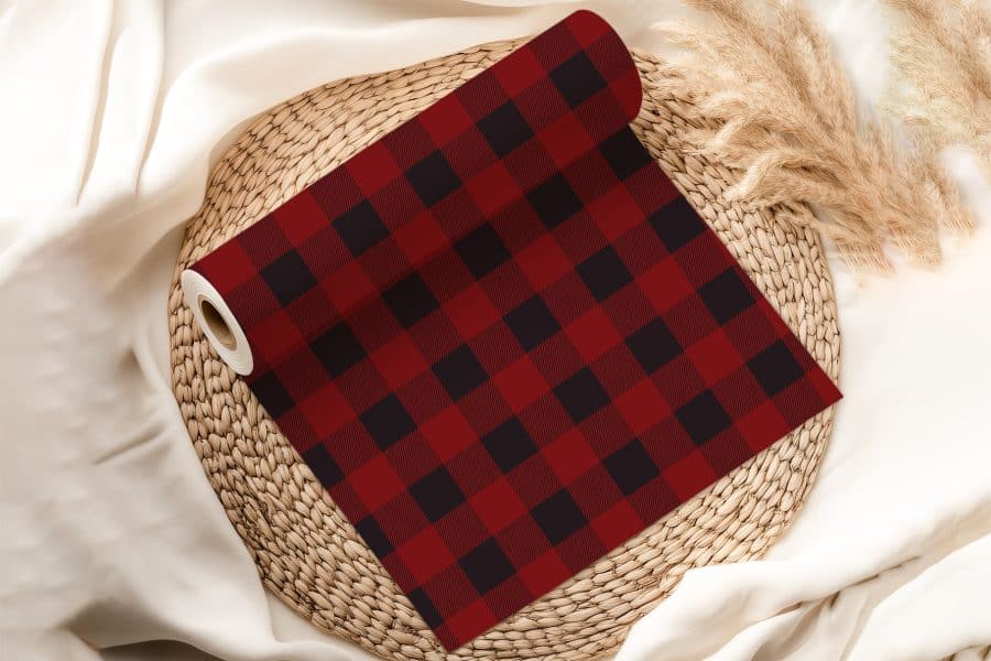 A Roll Of Red And Black Buffalo Plaid Fabric Rests On A Woven Mat.