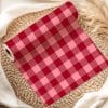 Roll Of Red And Pink Gingham Fabric On A Woven Mat.