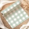 A Roll Of Sage Green And White Gingham Wrapping Paper On A Woven Placemat.