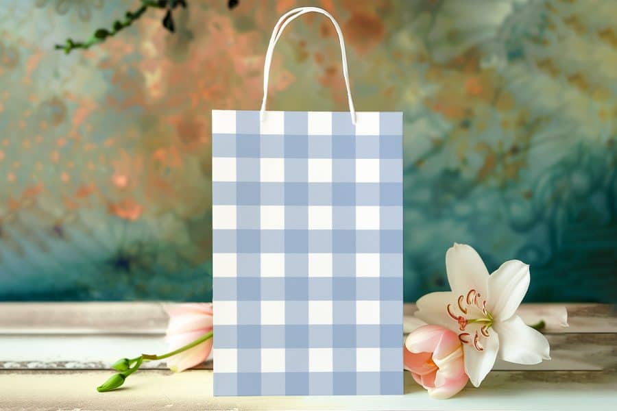 A Light Blue And White Gingham Gift Bag Sits On A Wooden Surface Next To Pink Tulips And A White Lily.