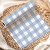 A Roll Of Light Blue And White Gingham Fabric Sits On A Woven Mat.