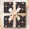 A Gift Wrapped In Dark Gray Paper Featuring A Repeating Pattern Of Candy Corn, Tied With A Beige Ribbon.
