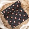 A Roll Of Dark Gray Fabric With A Repeating Pattern Of Candy Corn Sits On A Woven Placemat.