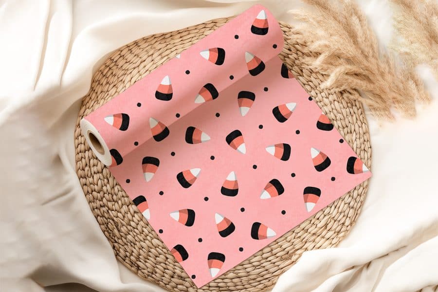 Pink Wrapping Paper With A Repeating Pattern Of Candy Corn Rests On A Woven Placemat.