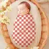 Sleeping Baby Swaddled In A Coral And White Checkered Receiving Blanket.