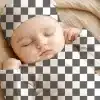Sleeping Baby Wearing A Checkered Onesie And Hat.