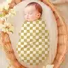 Sleeping Baby Swaddled In A Gold And White Checkered Blanket Inside A Wicker Basket.