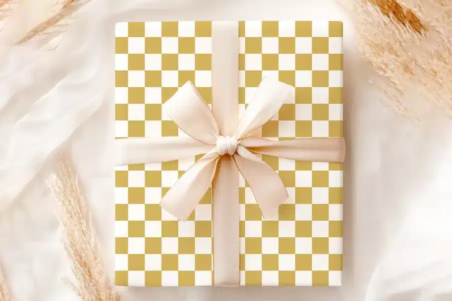 A Gift Box With A Gold And White Checkered Pattern And A Beige Ribbon.