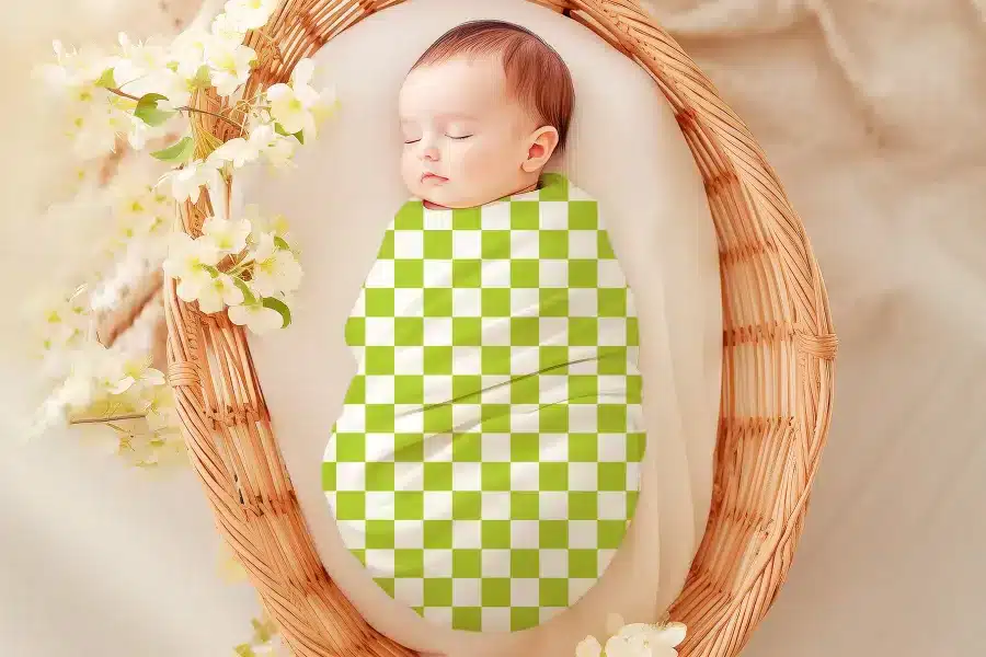 Sleeping baby swaddled in a lime green and white checkered blanket.