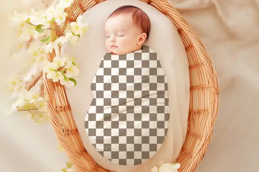 Sleeping baby swaddled in a checkered receiving blanket inside a wicker basket.