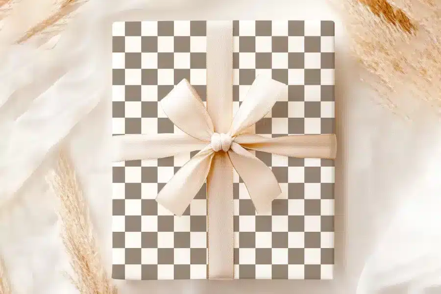 A Gift Box With A Taupe And White Checkered Pattern And A Large Beige Bow.