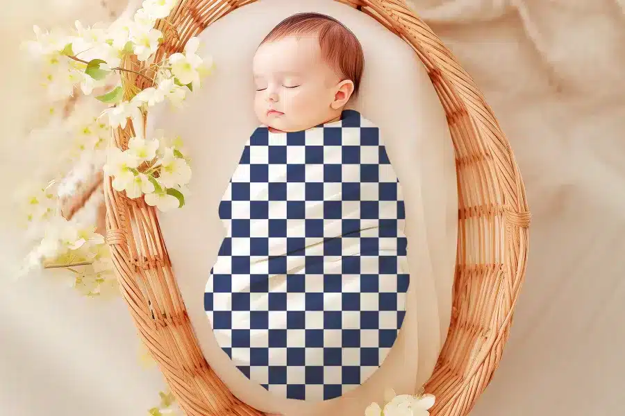 Sleeping baby swaddled in a navy and white checkered receiving blanket.